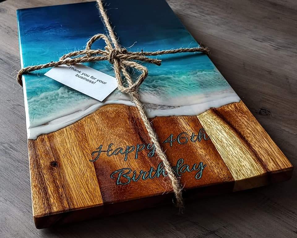 Wooden cutting board with 'Life is Beach, Enjoy the Waves' text on a kitchen counter with fruit and wine.