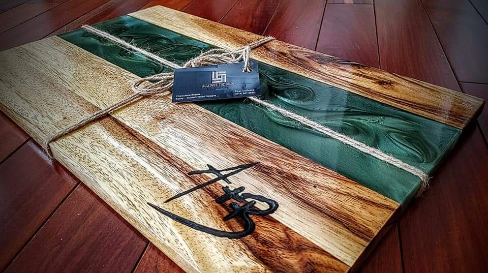 Wooden cutting board with a scenic design on a kitchen counter with wine and snacks.